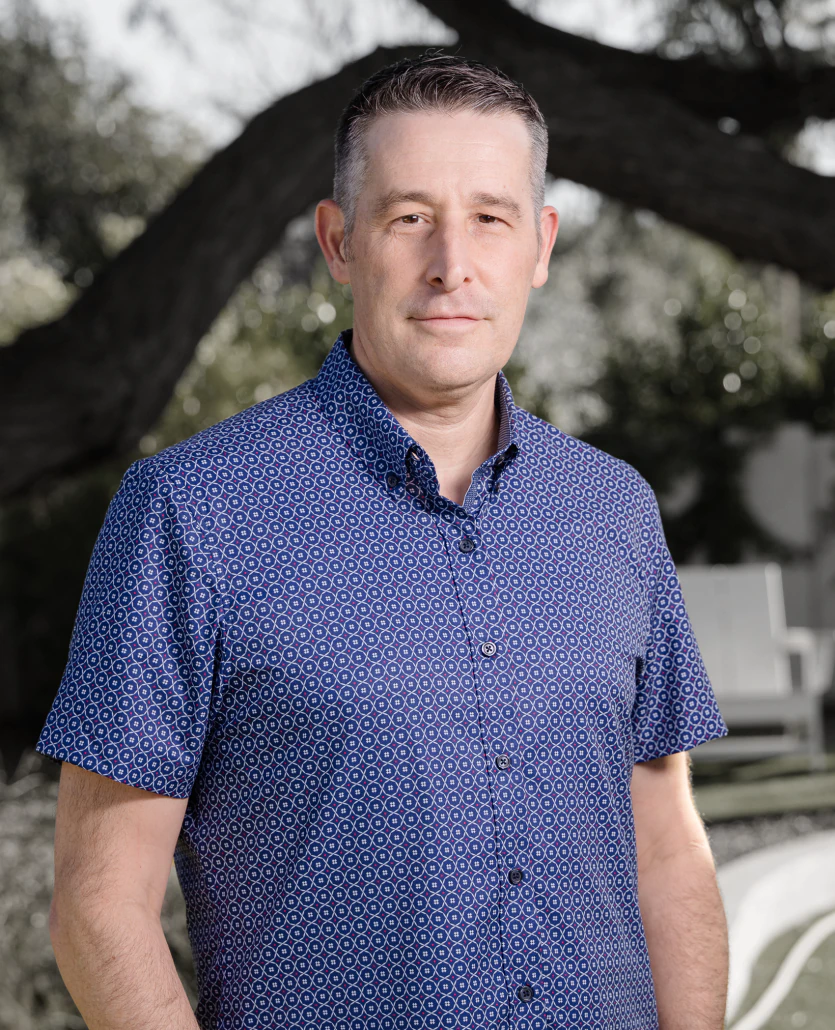 Ira Bernstein, Master Trained Facilitator of Selling Through Curiosity™, standing outdoors in a patterned blue shirt, promoting tailored sales training workshops.